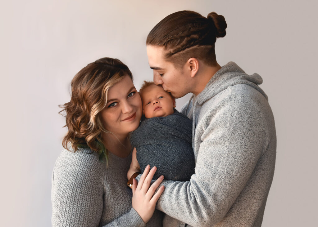 studio newborn session, family of 3 with close faces, dad kissing baby