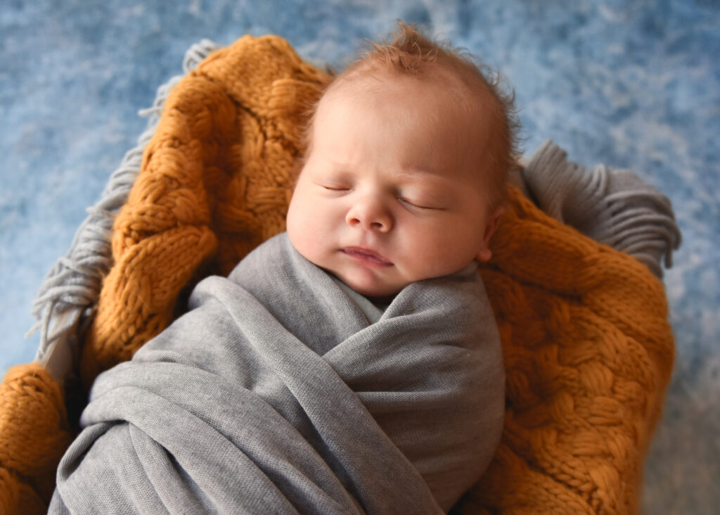 studio newborn session, baby boy on blue background with yellow blanket