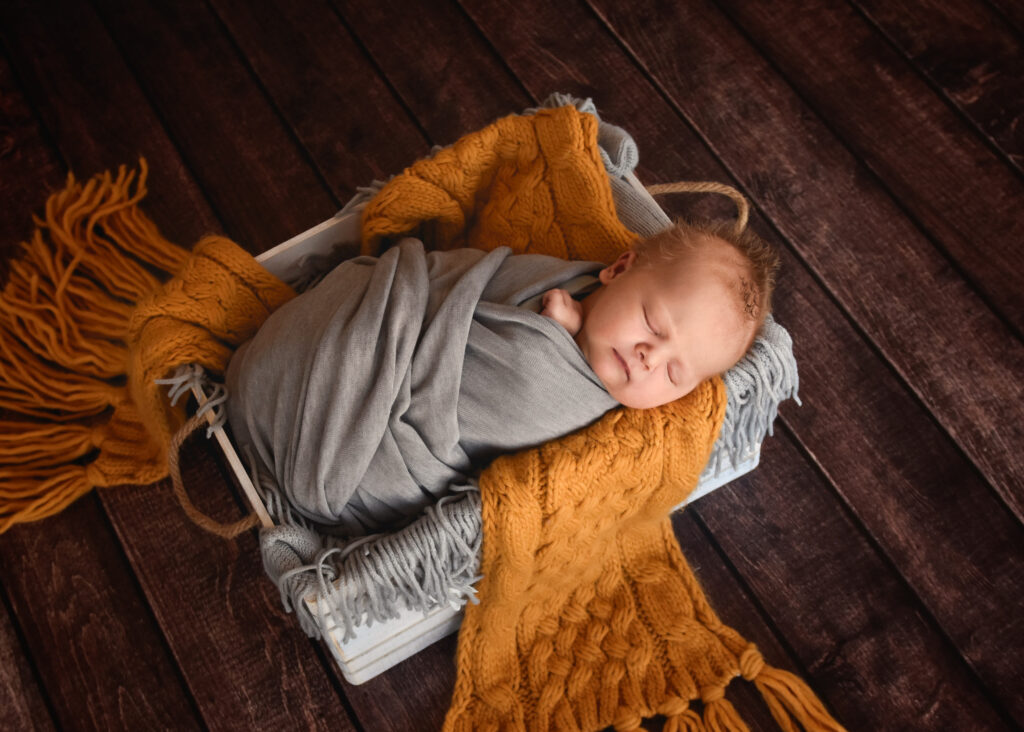 studio newborn session, baby wrapped in grey in white box with yellow blanket