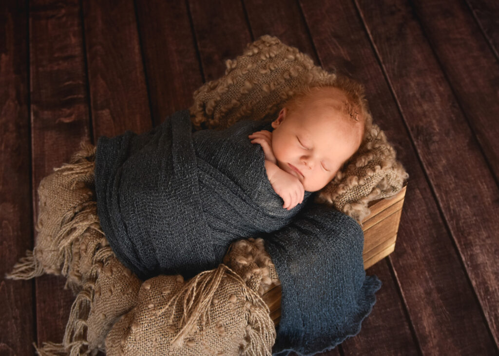 studio newborn session, sleeping baby boy wrapped in dark blue on earth tones