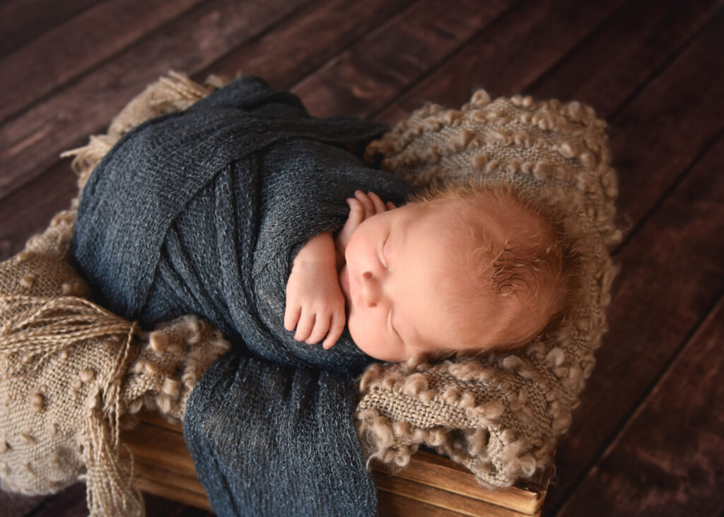 baby in blue wrap with hand out and curly hair