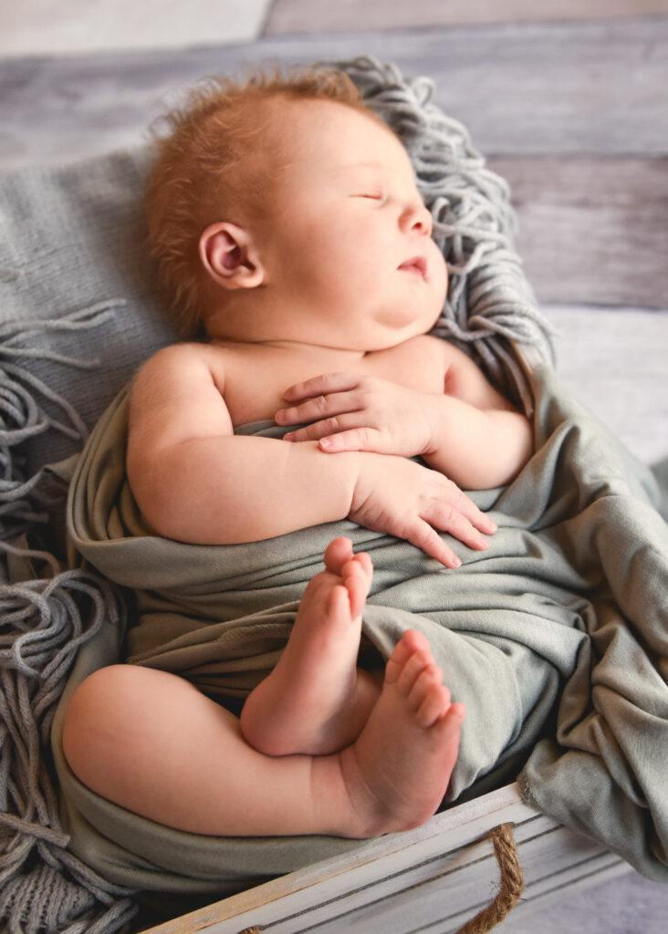 baby with curly hair on grey background in grey wrap